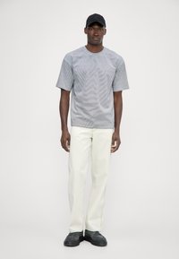 Camiseta a rayas grises, de mangas cortas y cuello redondo; combinada con pantalones rectos en color blanco roto y zapatos negros. Gorra negra sencilla en la cabeza.