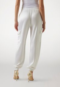 Vita satin joggerbyxor med elastiska muddar och midja, utrustade med två sidofickor. Bärs med guldiga stilettklackar.