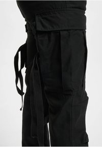 Black cargo pants with a relaxed fit, featuring multiple pockets, adjustable fabric ties, and a smooth texture. Details include side seams.