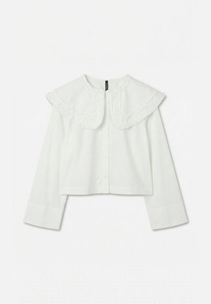 Blouse courte blanche à manches longues avec grand col rond à volants et fermeture par boutons sur l'avant, sur fond uni.