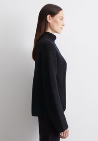 Schwarzer Rollkragensweater mit strukturiertem Strickdesign, überschnittenen Schultern und langen Ärmeln, der einen entspannten, kastigen Schnitt aufweist.