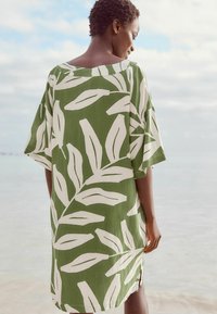 Vihreä lyhythihainen mekko, jossa on valkoinen lehtikuosi, kevyt kangas, löysä istuvuus ja sivuhalkiot mukavuutta varten.