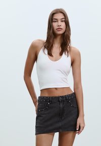 Top à fines bretelles blanc ajusté avec un large décolleté, associé à une mini-jupe en denim noir avec des clous en argent sur la ceinture et les poches.