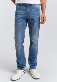 Jeans de mezclilla azul claro con un diseño de pierna recta, ligera decoloración y acentos bordados, combinados con zapatillas blancas.