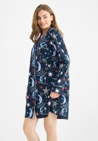 Navy pajama shirt featuring a celestial print of stars, moons, and planets, with a button-up design and a chest pocket. Soft fabric texture.
