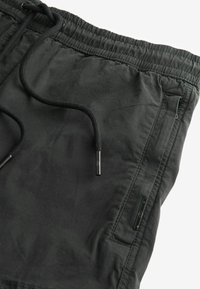 Black elasticated pants with a drawstring, featuring a smooth texture, side pocket, and contrasting black hardware accents.