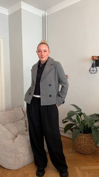 Pilkas dvieilis vilnos mišinio švarkas su juodais mygtukais, dėvimas ant juodo polo. Taip pat matomos laisvos juodos kelnės ir masyvūs juodi batai.