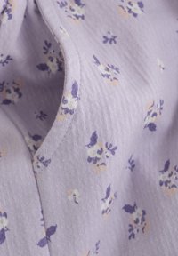 Ljuslila tyg med en mjuk textur, med ett blommönster i lila och persikofärgade nyanser. Synliga sömdetaljer längs kanterna.