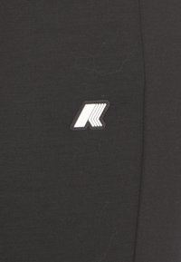 Leggings sportivi neri con una texture liscia e elastica, dotati di una patch logo bianca sul lato sinistro. Design semplice senza motivi.