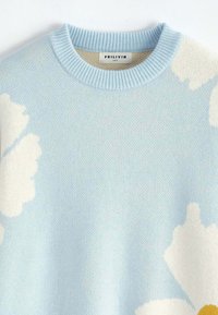 Pull en tricot bleu clair avec des motifs floraux blancs et un col rond côtelé, étiquette taille M de la marque Frilivin.