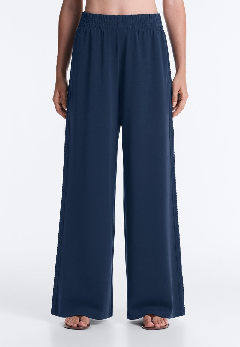 Femme portant un pantalon large bleu marine ample avec une taille élastique, debout pieds nus sur un fond blanc.