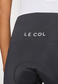 Schwarze Radsportshorts mit gepolsterter Sohle, 'LE COL'-Logo in Weiß, glatte Textur und Flachnaht für Komfort.