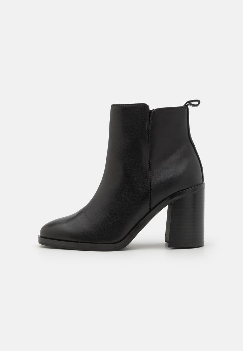 Bottine noire en cuir avec talon bloc et languette latérale, finition lisse et bout arrondi, présentée sur un fond blanc uni.