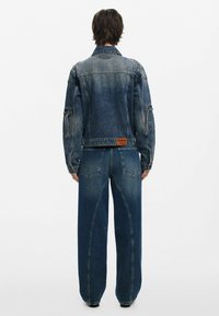 Džínová bunda a široké nohavice vo vyblednutej modrej farbe. Bunda má vrecká a štítok; nohavice majú charakteristické prešívanie a zadné vrecká.