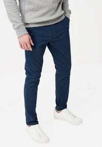 Chinos bleu marine à coupe slim, en tissu coton. Associés à des baskets blanches et un pull gris avec des poignets côtelés.