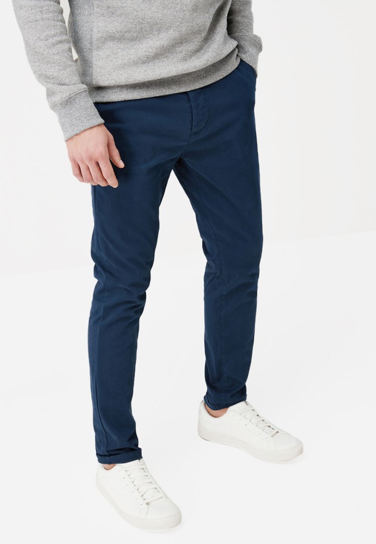 Chinos bleu marine à coupe slim, en tissu coton. Associés à des baskets blanches et un pull gris avec des poignets côtelés.