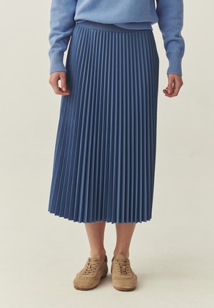 Plisseret midi-nederdel i ensartet blå, lavet af letvægtstof. Har en bred taljebånd og falder under læggen, kombineret med beige sneakers.