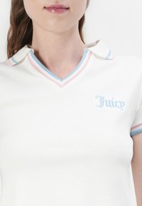 Bijela polo majica kratkih rukava s V-izrezom, s ovratnikom i manžetama u pastelnim plavim, ružičastim i svijetloplavim prugama, izvezeni logo "Juicy".