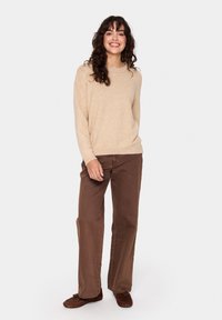 Beežist lõngast kudum, millele on lisatud pehme tekstuur, koos lõtvade pruunide pükstega. Riietus on lõpetatud pruunide mokassi stiilis kingadega.