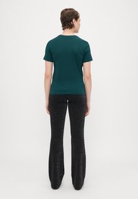 T-shirt ajustada verde-água com mangas curtas, combinada com calças pretas largas que apresentam um suave brilho metálico e um tecido texturizado.