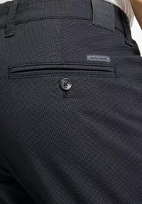 Czarne spodnie o fakturze, z tylną kieszenią z zapięciem na guzik oraz metką z napisem "CROSS JEANS". Tkanina ma subtelny wzór.