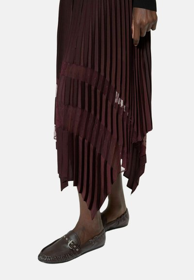 Persona de piel oscura que lleva una falda plisada burdeos con detalles de encaje y zapatos de cuero marrón oscuro sin cordones con una hebilla.