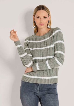 Grauer, kabelgestrickter Pullover mit weißen Streifen, gerippten Bündchen und Saum. Das Model trägt den Pullover mit dunklen Jeans und auffälligen Ohrringen.