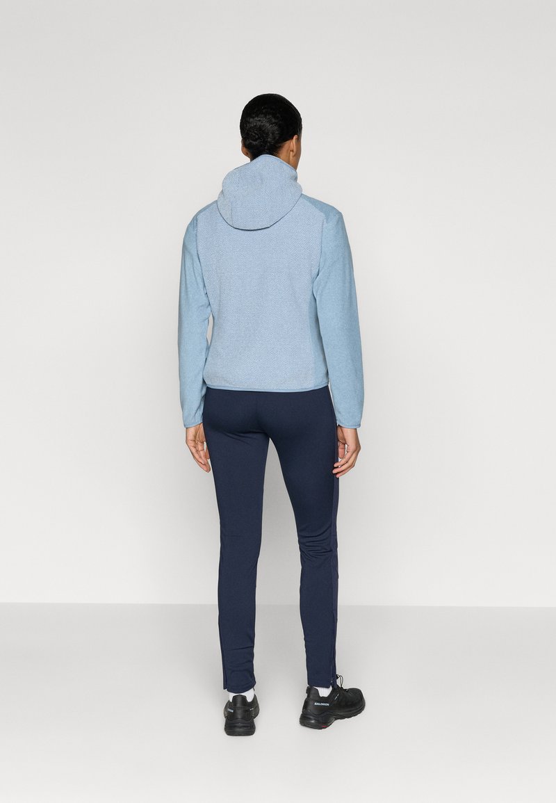 Jasnoniebieska kurtka z kapturem o teksturowanym wzorze, w połączeniu z granatowymi dopasowanymi spodniami i czarnymi sneakersami, widok z tyłu.