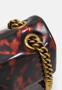 Handväska med sköldpaddsmönster och glänsande yta, utrustad med kedjeband i guldton och prägling av logotyp på en metallögla.