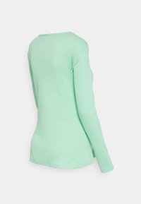 Camisa de manga longa verde-menta clara, feita de algodão canelado, apresenta um corte redondo e uma forma ajustada com uma textura suave.