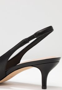 Czarny skórzany but na obcasie typu slingback z wąskim obcasem, odkrytym palcem i teksturowanym paskiem, o gładkim wykończeniu i beżowej wkładce.