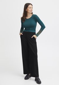 Türkiz hosszú ujjú felső csipkés díszítéssel, széles szárú fekete nadrággal és fekete slip-on cipővel párosítva. Simább textúra az egész területen.