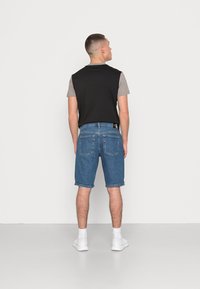 Top de manga corta en negro y gris combinado con pantalones cortos de mezclilla azules. Zapatillas deportivas blancas. Diseño simple con ajuste corto y pantalones cortos con dobladillo.