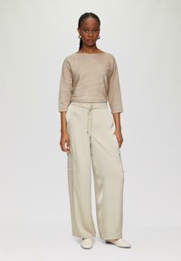 Beżowy sweter dzianinowy z białym wzorem, trzyczwarte rękawy, w połączeniu z luźnymi beżowymi spodniami cargo i kremowymi butami wsuwanymi.