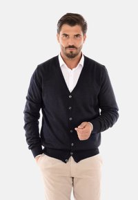 Cardigan blu navy in morbido filato, con scollo a V, sei bottoni e polsini a coste. Abbinato a una camicia bianca con colletto.