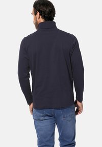 Navyblaues Langarmhemd mit hohem Kragen, aus weichem Stoff gefertigt. Die Details umfassen einen geraden Schnitt und minimale Stichakzente.