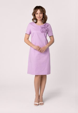 Robe lilas à manches courtes, coupe droite, ornements floraux sur l'épaule gauche, associée à des chaussures blanches à lanières.
