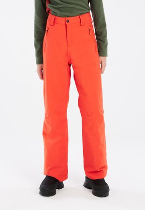 Pantaloni da neve arancioni con una texture liscia, tasche con zip e vita alta. Abbinati a stivali neri isolati per il freddo.