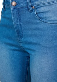 Vaqueros de mezclilla azul con una cintura alta, diseño minimalista, ligero desvanecimiento y un botón de bronce con detalle del logotipo.