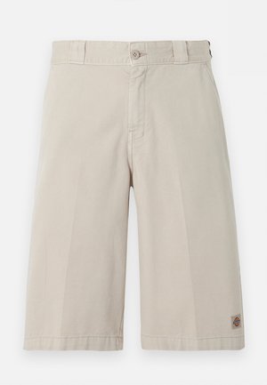 Beige knee-length shorts with button and zipper closure, belt loops, and a small logo patch near the bottom hem on the right leg.
