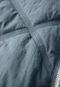 Teksturowana, ciemnoniebieska tkanina z wyszywanymi wzorami i widocznym zamkiem. Charakteryzuje się pomarszczonym wyglądem i starannym wykończeniem szwów.