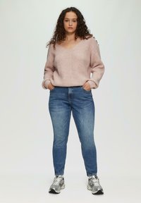 Suéter de punto rosa claro con escote en V y corte holgado, combinado con unos jeans ajustados azul y zapatillas deportivas plateadas.