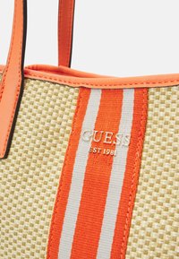 Sac fourre-tout tissé en tan avec un accent rayé orange et blanc. Présente un logo argenté en relief, des bordures orange et deux poignées robustes pour les épaules.