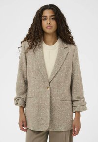 Bež blazer z teksturo, ki ima herringbone vzorec, en gumb za zapiranje in dve sprednji žepek; sproščen kroj z zavihanimi rokavi.