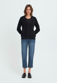 Cardigan negro de canalé con escote en V, cierre de botones y mangas largas, combinado con jeans azules recortados y mocasines negros.