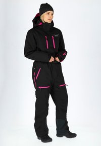 Black insulated winter suit with pink zippers and accents. Features a hood, multiple pockets, and textured black fabric.