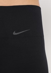 Czarne legginsy sportowe z prążkowaną strukturą i małym szarym logo Nike na pasku, zaprojektowane z myślą o komforcie i elastyczności.