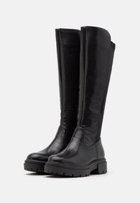 Bottes noires montantes en matériau texturé avec une finition lisse, dotées d'une semelle en caoutchouc épaisse et de détails de couture minimalistes.