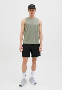 Haut de sport sans manches vert en tissu anti-humidité, associé à un short noir avec cordon de serrage et logo. Chaussettes blanches et chaussures grises.