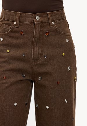 Jean en denim marron orné de bijoux multicolores. Design classique à cinq poches avec braguette à boutons et tissu texturé.